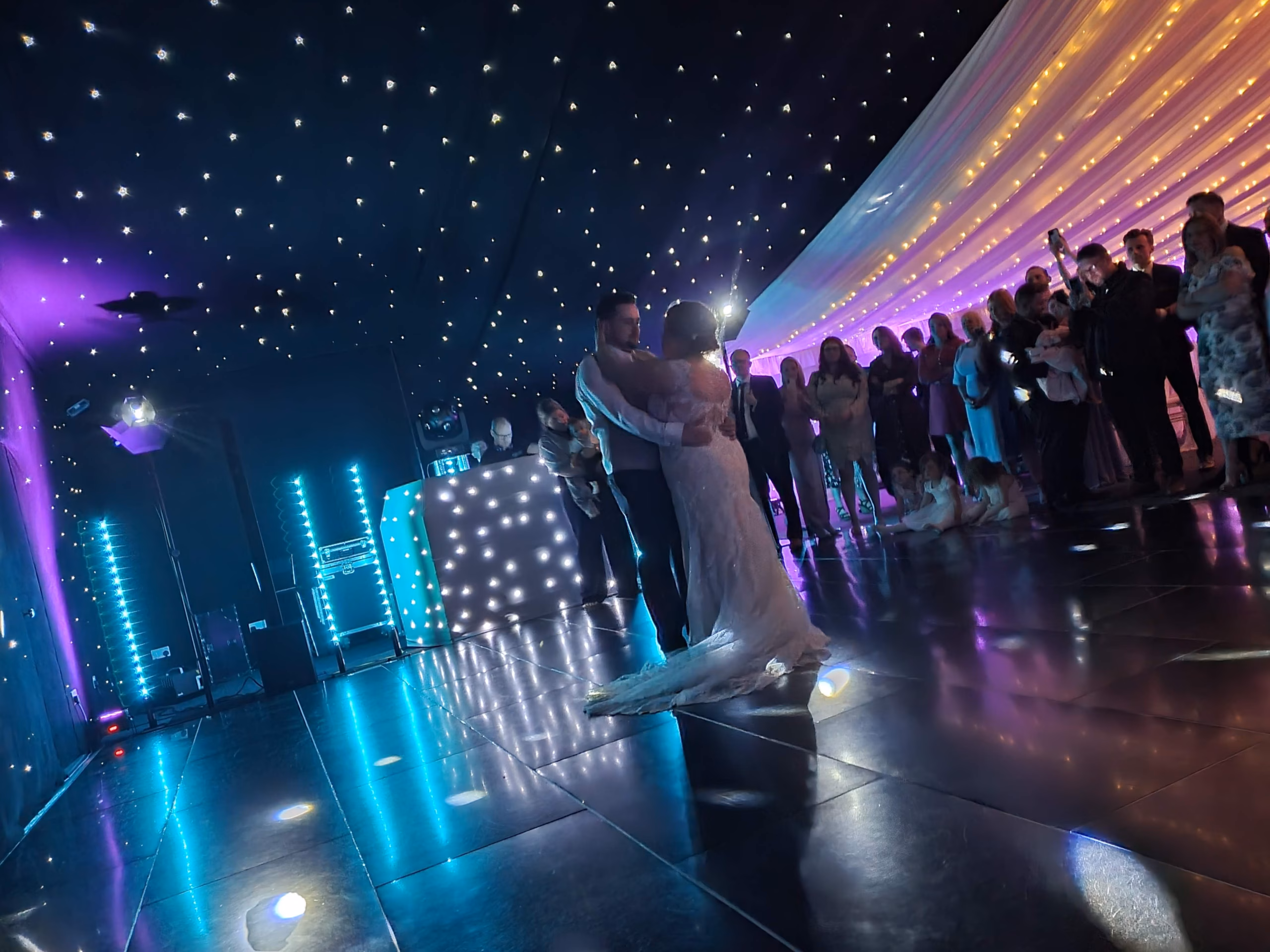 Real Wedding Chippenham Park Suffolk Modern wedding DJ setup with starlit dance floor, blue uplighting, and marquee star ceiling during a bride and groom's first dance.