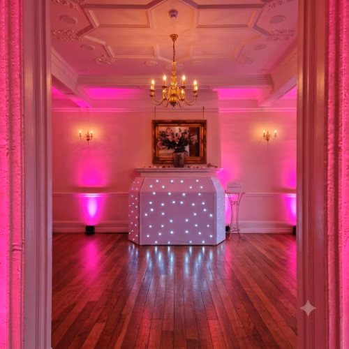 Elegant white wedding DJ booth with pink mood lighting at Lanwades Hall in Suffolk, provided by a professional wedding DJ serving Suffolk, Cambridgeshire and Norfolk.